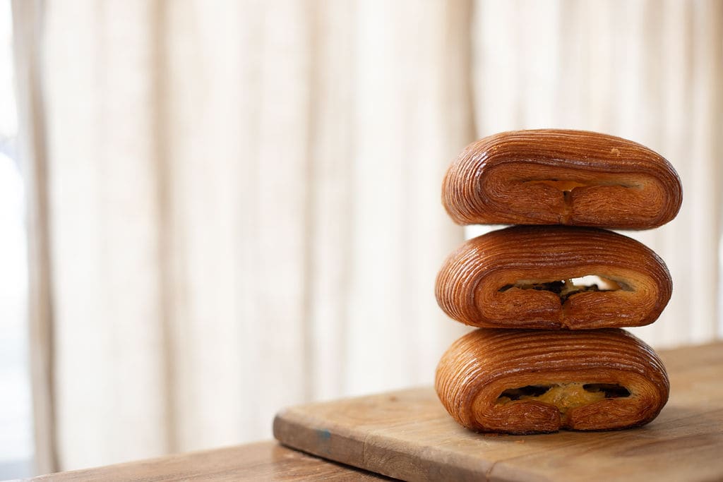 Three pains au chocolat stacked on a board, with soft light behind