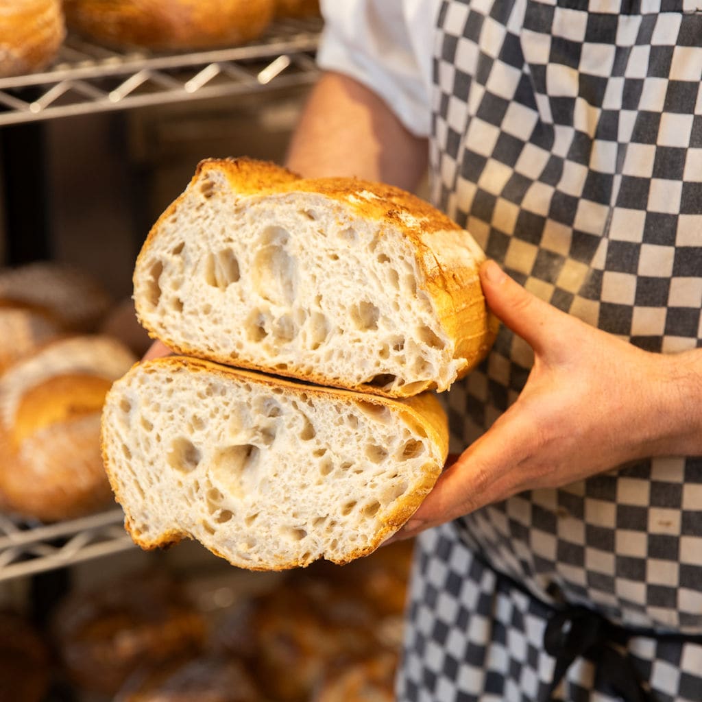A baker holding two halves of a sourdough loaf